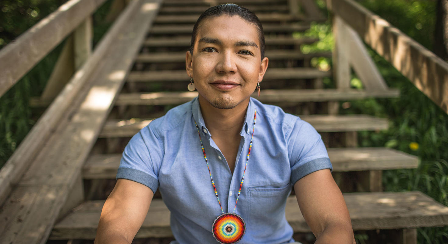 Portrait of James Makokis sitting on wooden steps outside