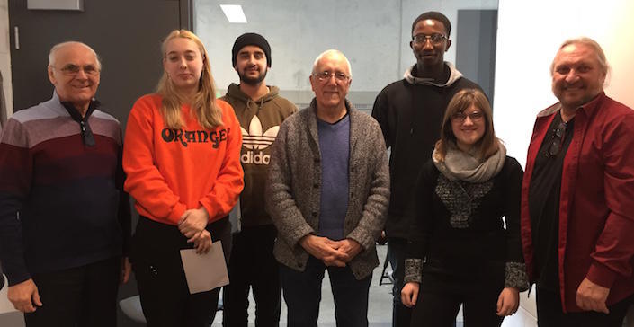 Five men and two women, smiling, stand in a classroom.