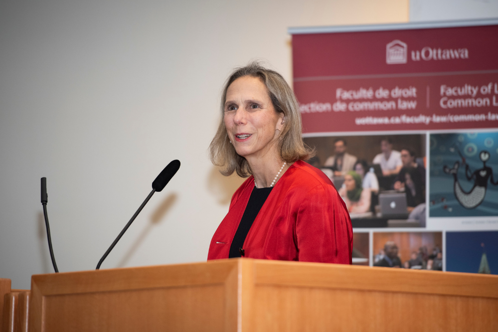 A woman wearing a red blazer speaks in front of a microphone