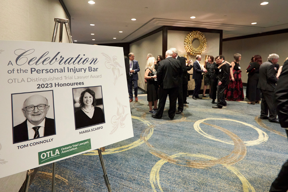 The entrance to a large ballroom or event room. There is a sign on the left indicating the guests of honour and many people in the room in black tie attire.