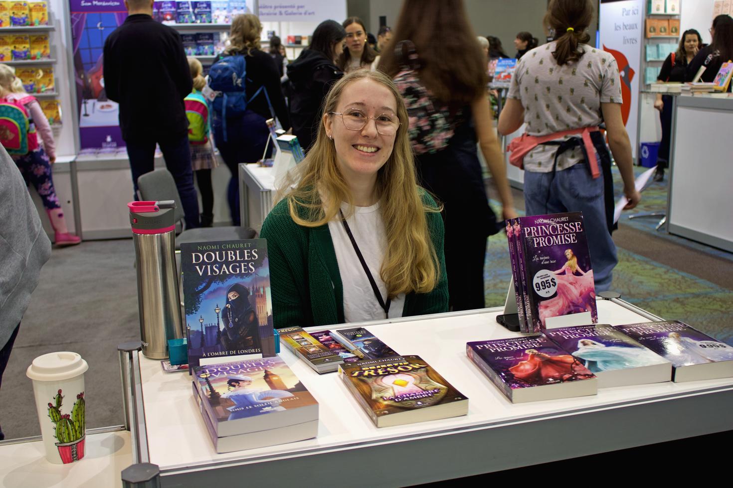 Portrait de Naomi Chauret entourée de ses livres à une séance de dédicace