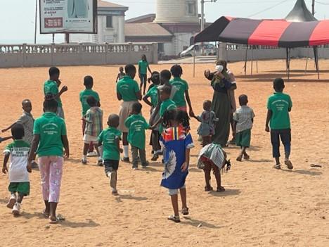 A group of kids wearing a green t-shirt and walking on the sand in a village