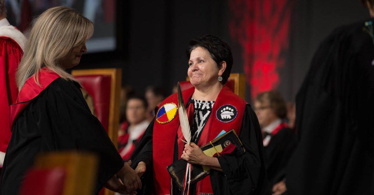  Student in graduation gown receives diploma at convocation.