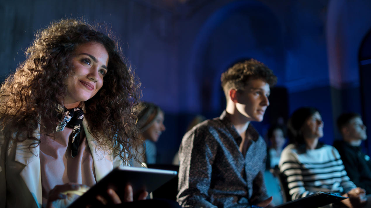 Members of an audience watch a show in a darkened theatre.