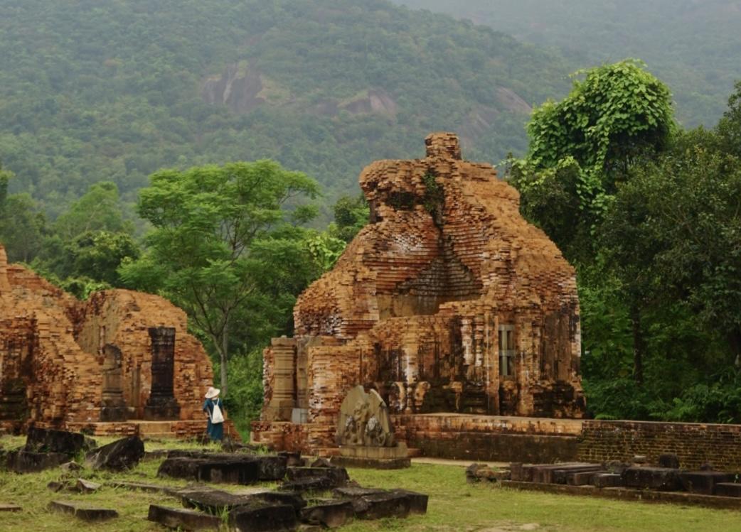 A forest and a mountain in the background. Brown big sculptures in the foreground on a field 