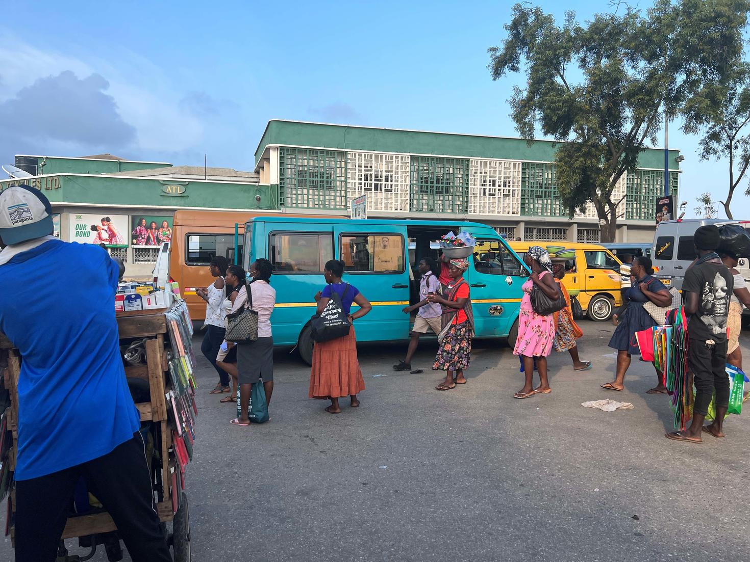 A group of people walking in the streets and passing in front of mini buses