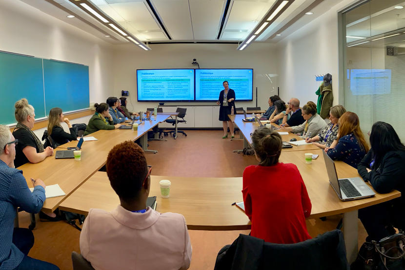 Conference participants sitting around table, listening to presentation