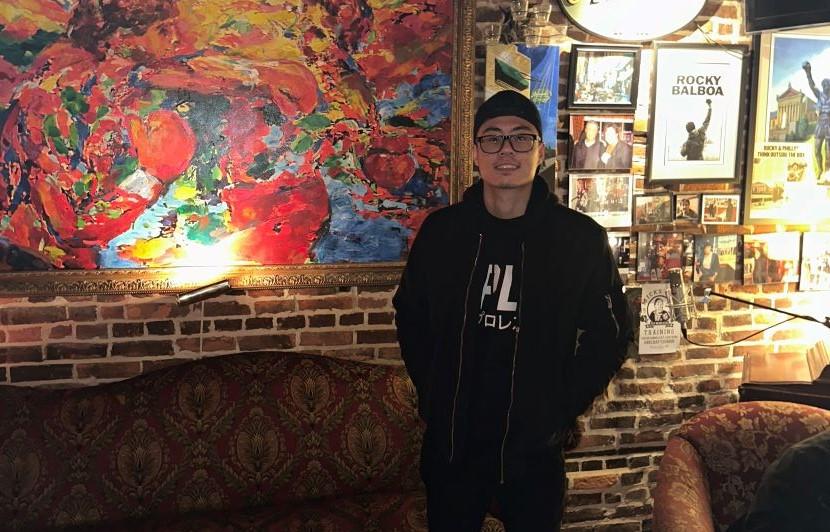 Student and DJ Richard Pham in front of a colourful painting inside a café.