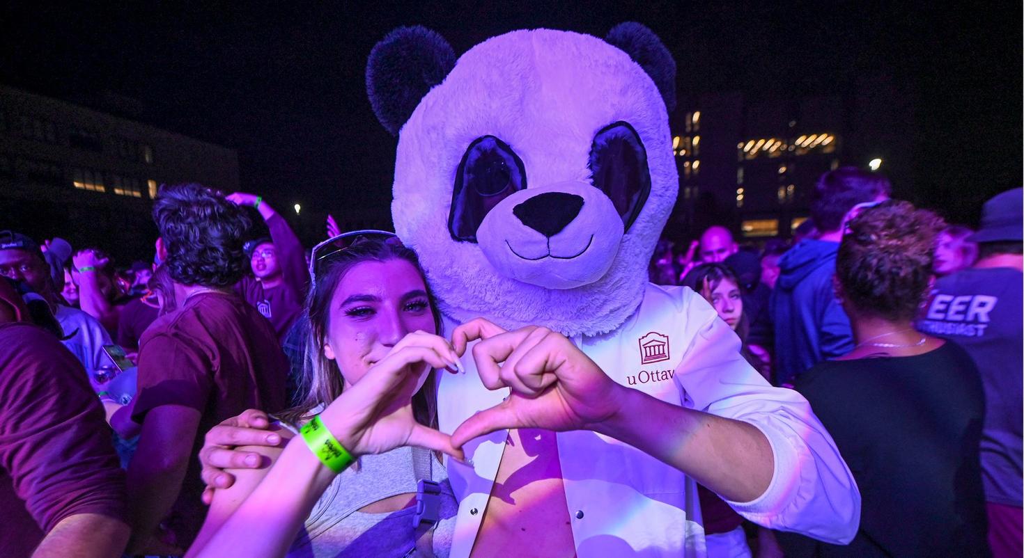 A student and another student wearing a Panda mask put their hands together to make a heart.