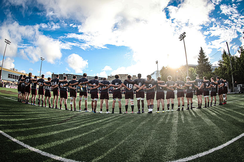 L'équipe masculine de rugby des Gee-Gees de l'Université d'Ottawa se tient bras dessus bras dessous au soleil sur le terrain de rugby.