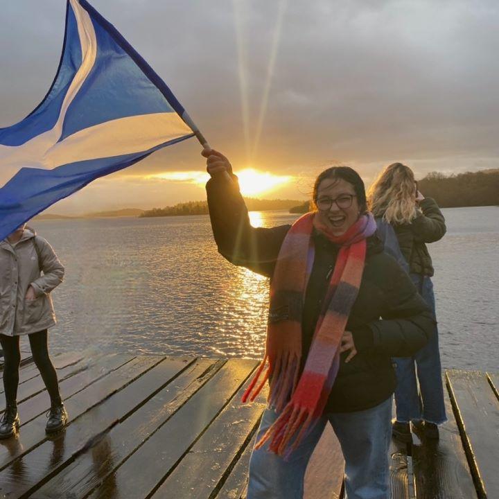 Emma Guzzo brandit un drapeau écossais alors que le soleil se couche sur un lac.