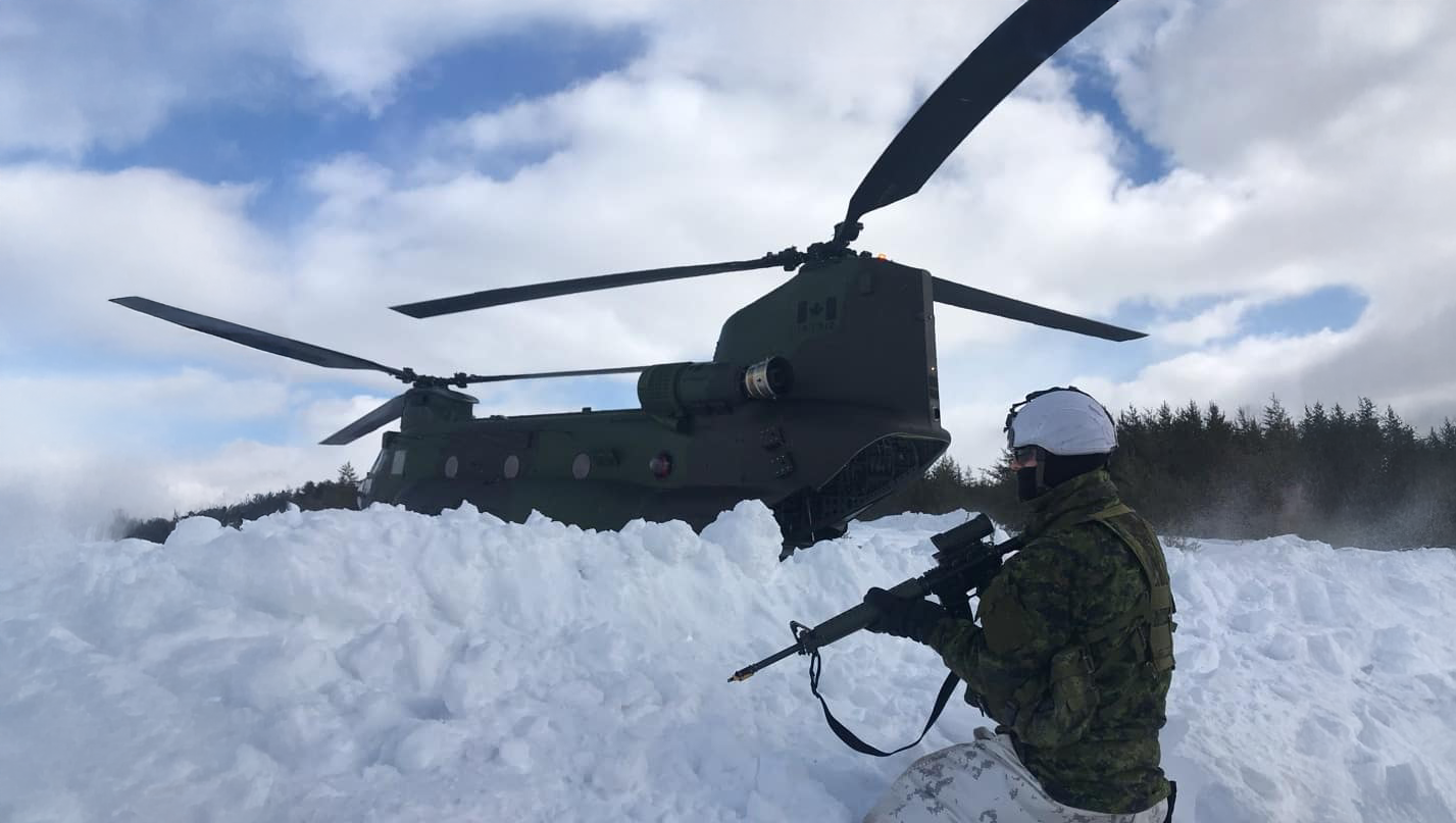 A soldier kneeling in the snow beside a helicopter