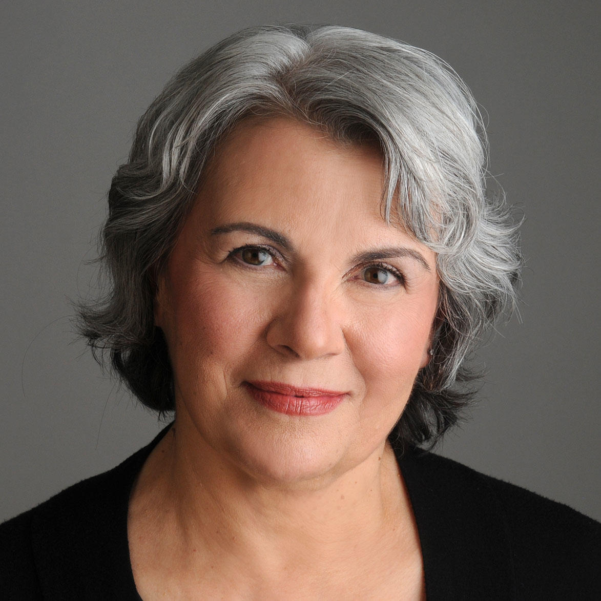 Portrait of Mary Ellis, a woman with short silver hair, a warm expression, and a black top against a neutral background.
