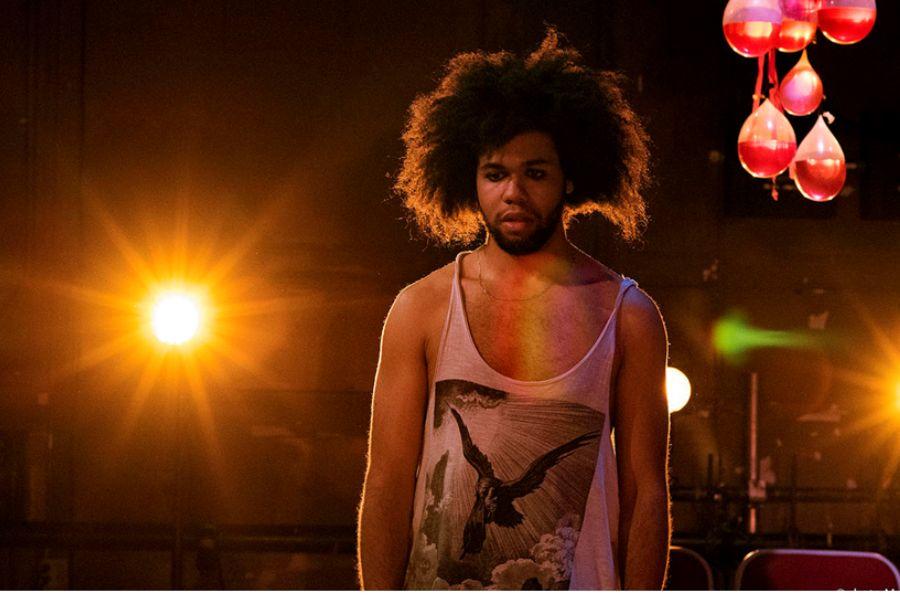 A man stands confidently in front of a bright light on stage.