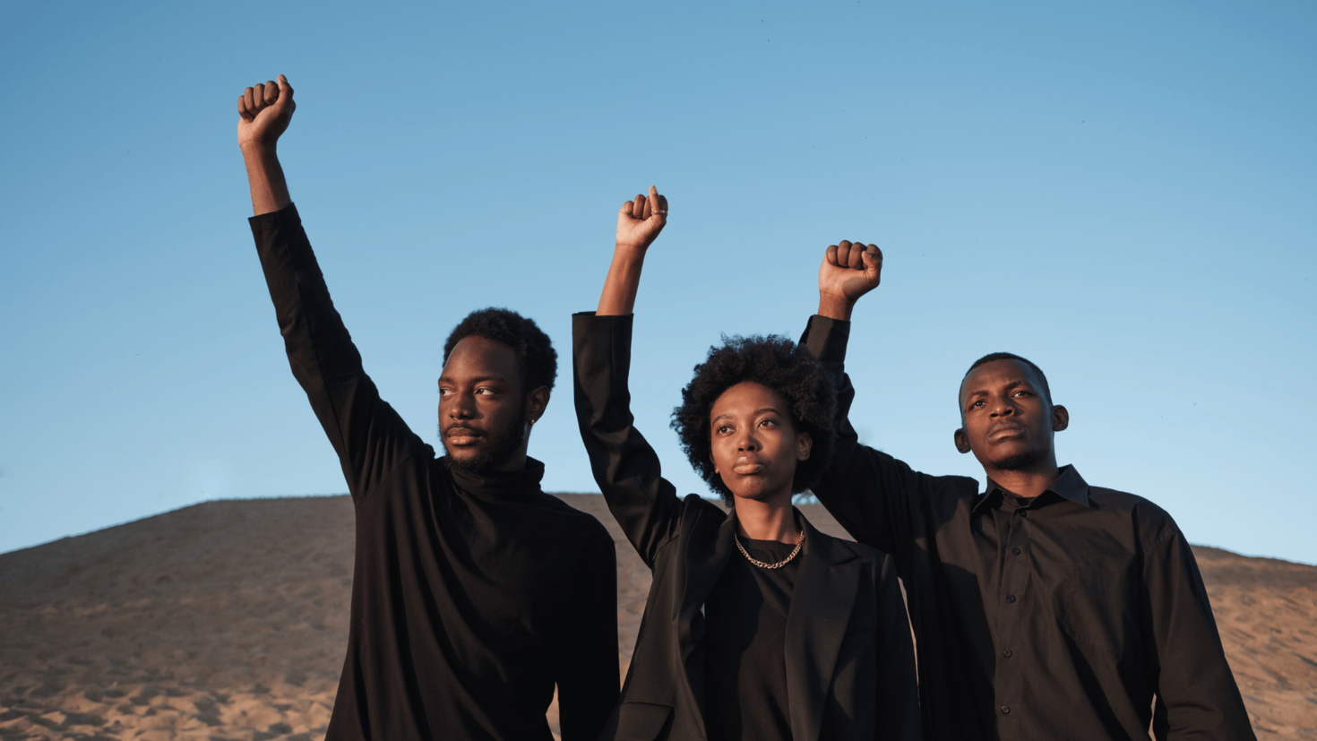 Three Black People in Black Outfit Raising Their Fist Outdoors