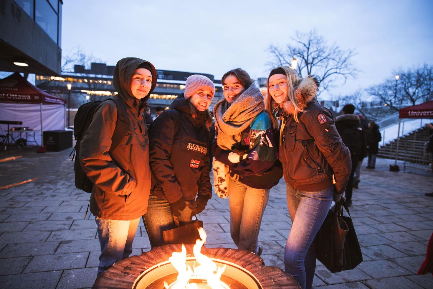 Four students warm up around a fire outdoors in the winter.