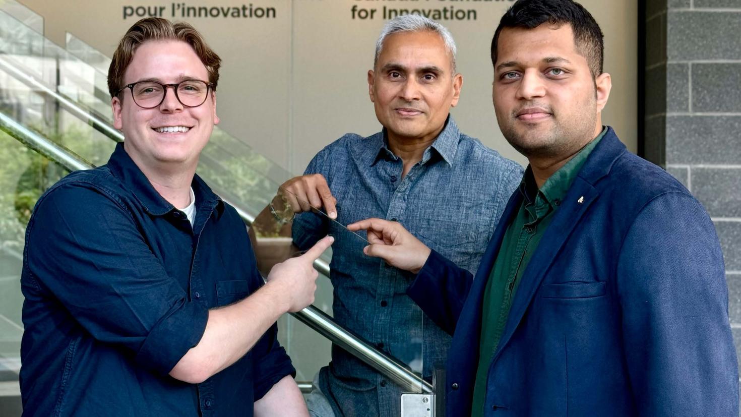 Jean-Luc Bégin, Professor Ravi Bhardwaj and Ashish Jain are standing in the uOttawa Advanced Research Complex, pointing to a glass railing. 