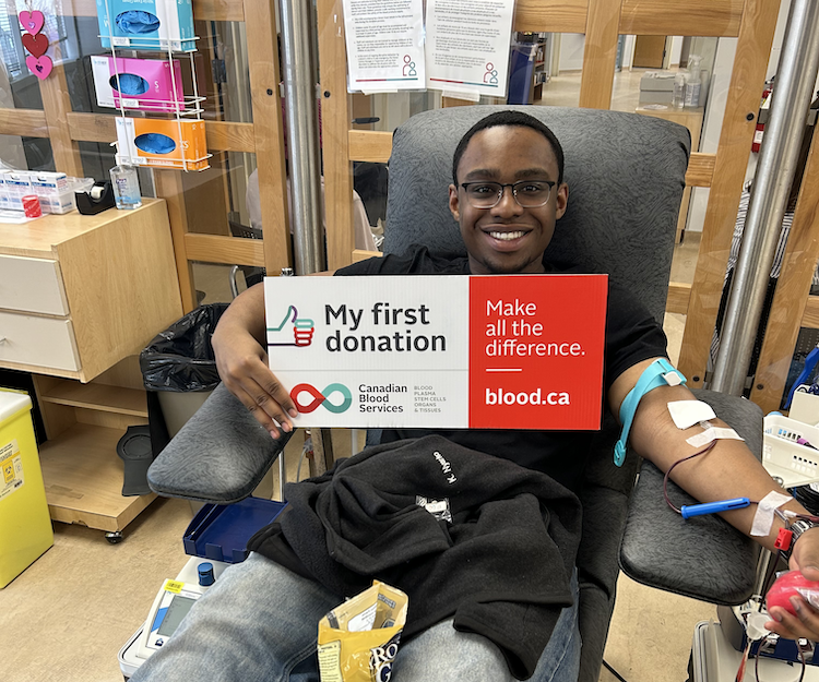 A blood donor holding a sign saying My First Donation