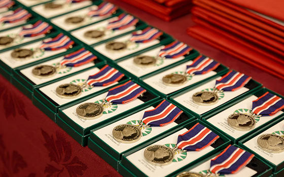 Several King Charles III Coronation Medals on a display. The medal is circular and silver in colour and  attached to a dark blue, bright red and white ribbon.