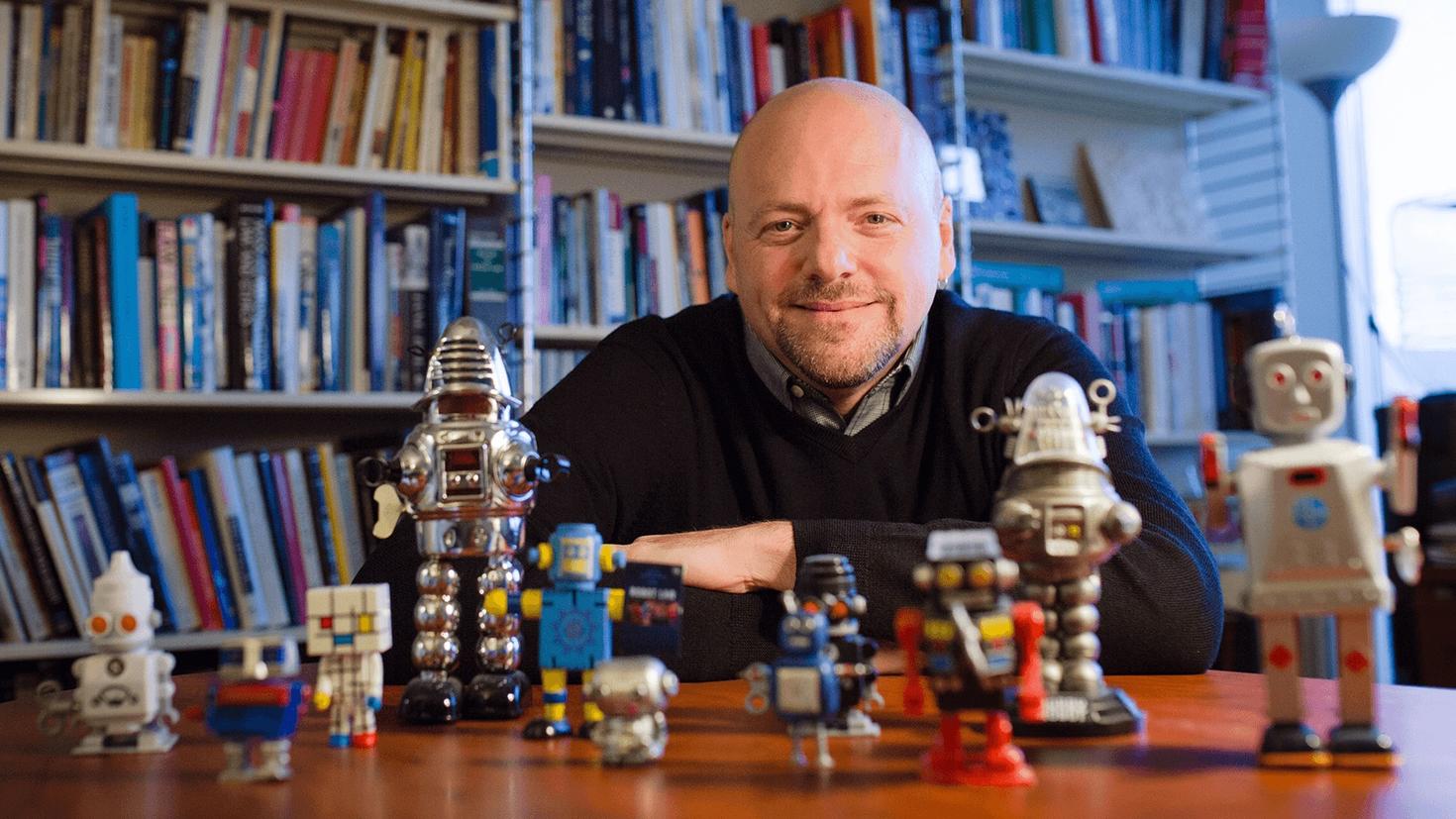 uOttawa professor Ian Kerr seated at the table with many little robots in the foreground.