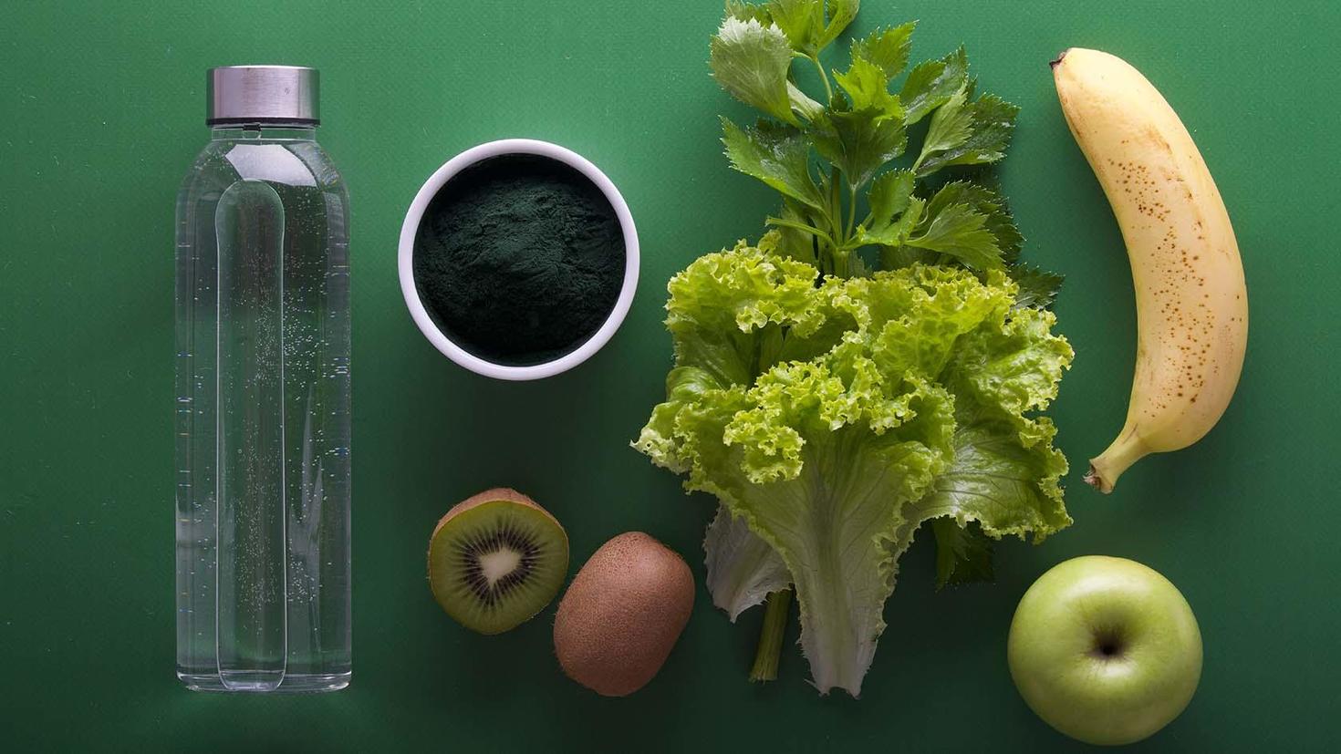 Fruits and vegetables with a water bottle on a green background