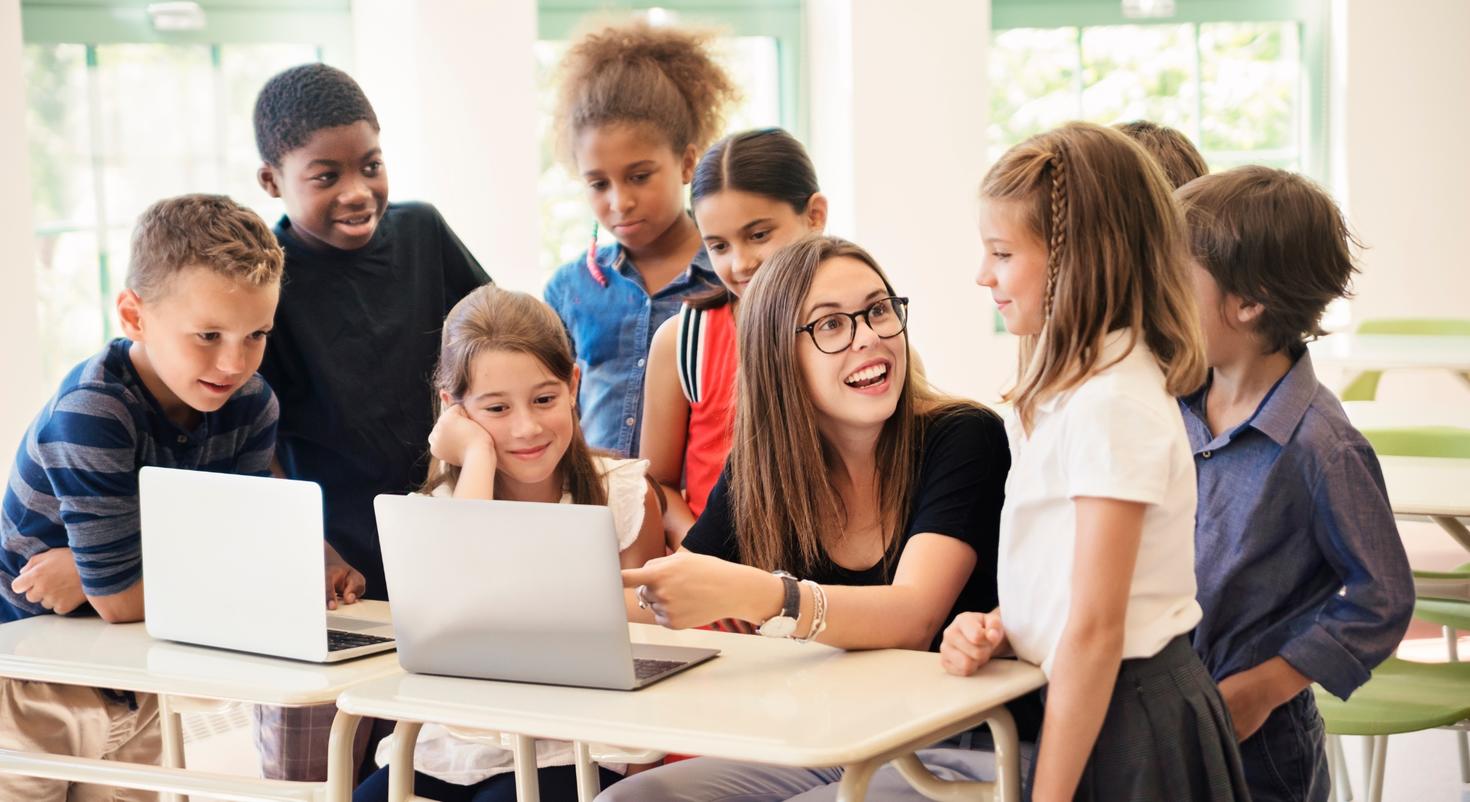 A teen showing a group of kids how to use a laptop.