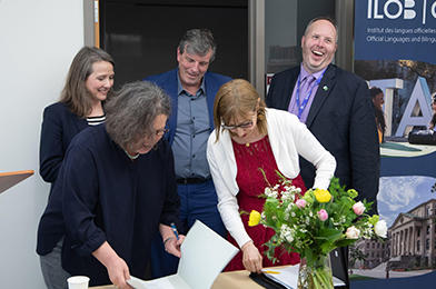 Catherine Buchanan signing a document surrounded by 4 other people.