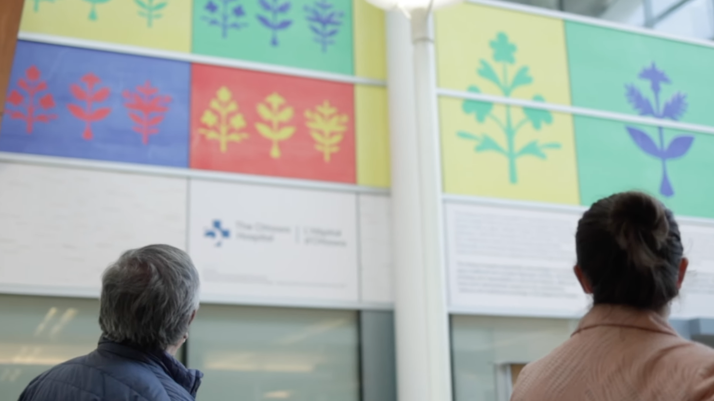 Simon Brascoupé and his daughter looking up at his art on display on a wall in The Ottawa Hospital