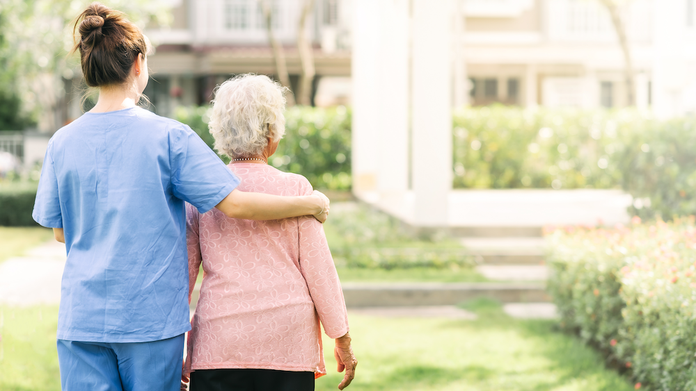 a medical professional guides an elderly patient through a garden.