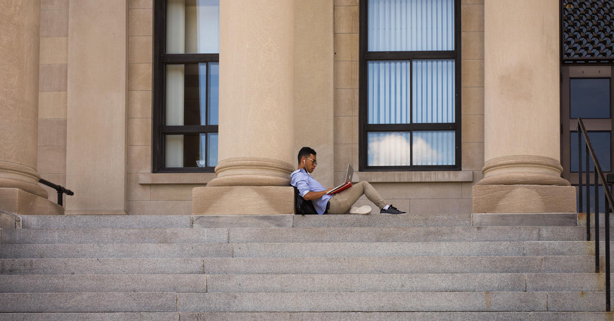 A student working on his laptop outside of Tabaret Hall