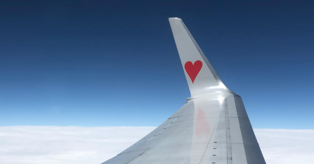 plane wing with red heart painted on it ,blue sky and clouds from passengers perspective