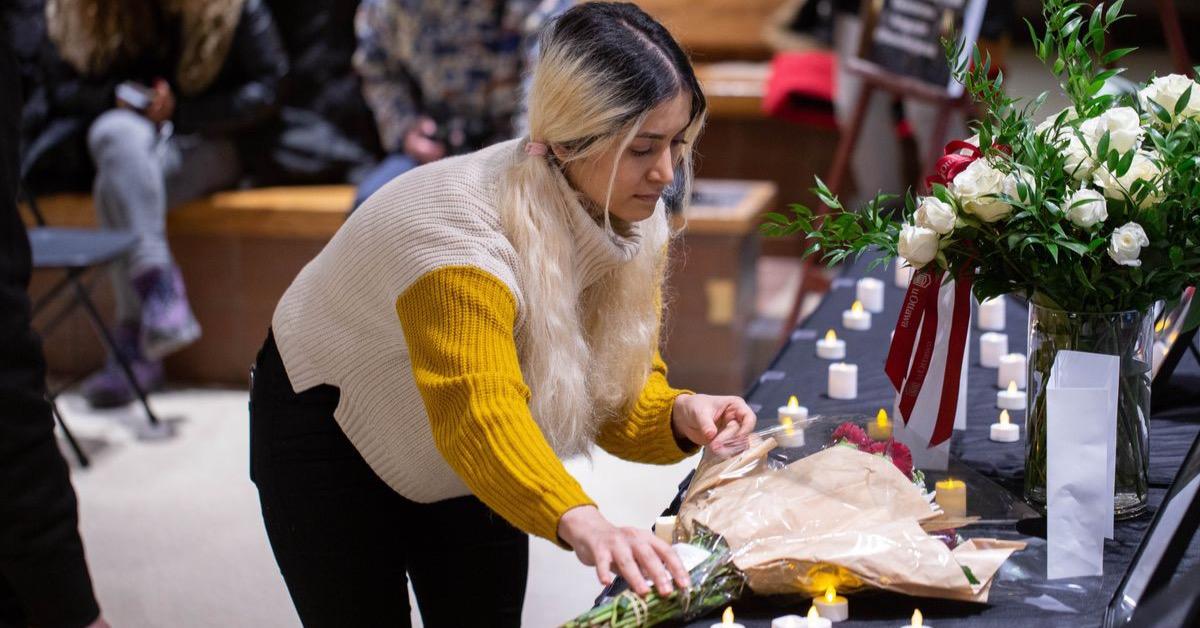A young woman lays a wreath of flowers on a memorial table