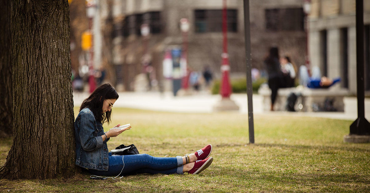 A women reads her book while sitting under a tree.