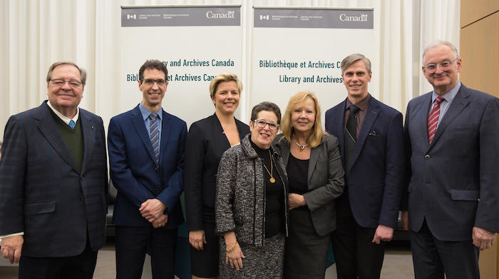 Four men and three women stand in front of a Library and Archives Canada backdrop.