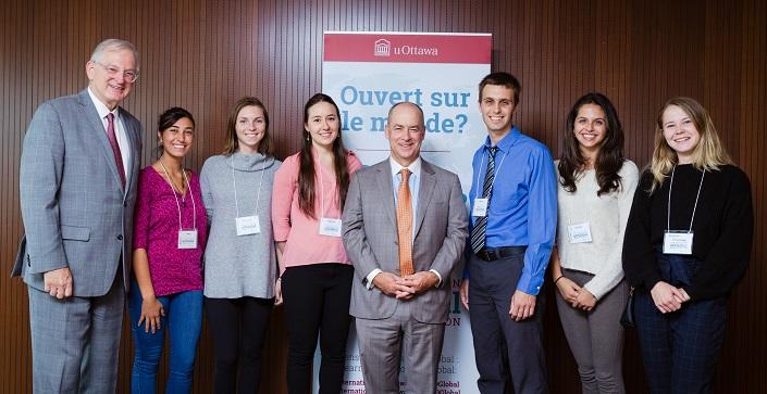 Six students stand in front of a banner with Jacques Frémont and Paul Genest.