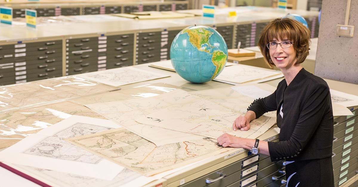 France Martineau stands in a map library reviewing centuries-old maps of North America.