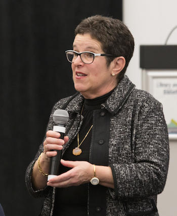 Anne Gilbert speaks, holding a microphone.