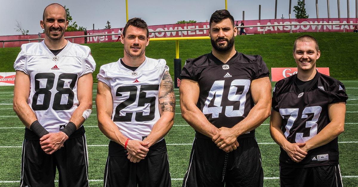Four football players stand side by side at center field.