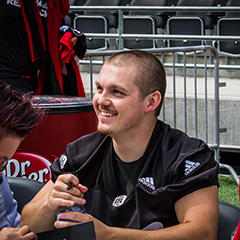 Lewis Ward sits at a table smiling signing autographs for fans.