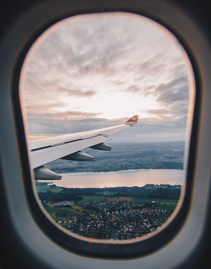 The wing of an aircraft seen from the plane against a cloudy sky, with a lake and a city below.