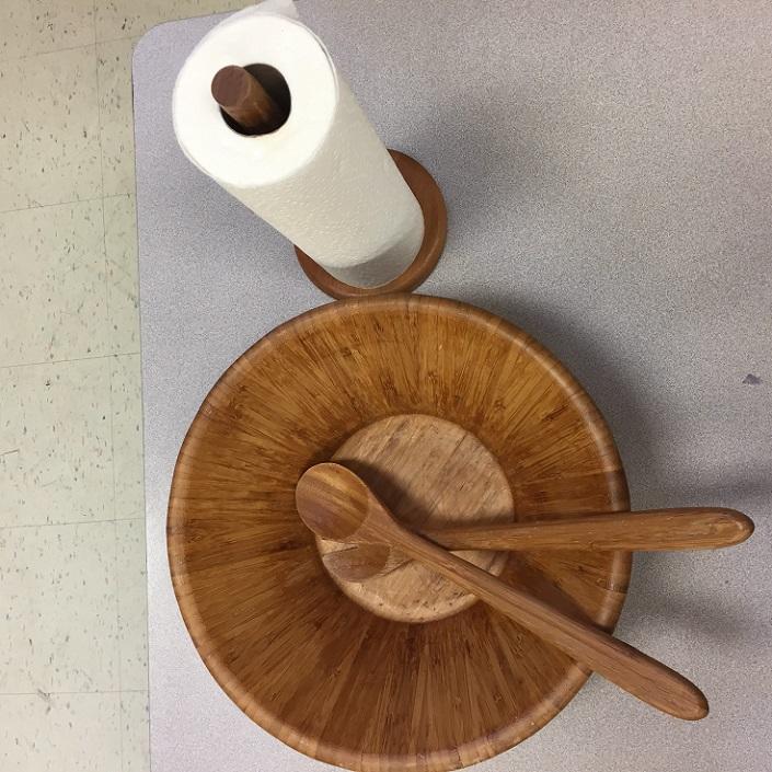 A wooden salad bowl with two spoons and a roll of paper towels.