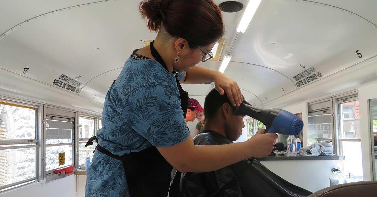 A volunteer hairdresser dries hair of a user.